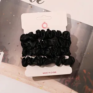 Set of 4 black satin scrunchies displayed on a white card against a warm background