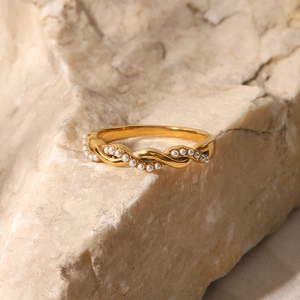 Close-up of golden twisted titanium steel ring with white pearl on stone texture