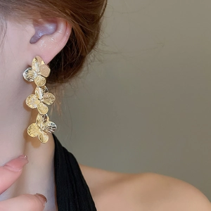 Close-up of golden clover-shaped long earrings worn by a model in natural soft lighting