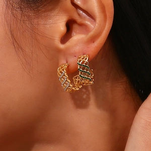 Gros plan de boucles d'oreilles dorées en maille C avec zircons verts et blancs