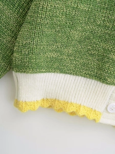 Detail of green knit sweater showing white ribbed hem and yellow scalloped crochet trim