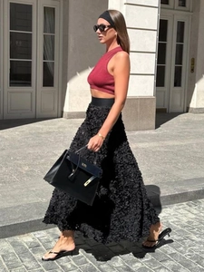 Detail of black maxi skirt with 3D petal texture and red knit crop top in urban setting