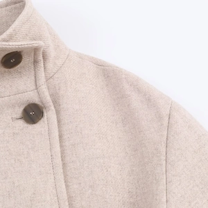 Dettaglio del tessuto in lana ad alta densità e del collo alto del cappotto color avena