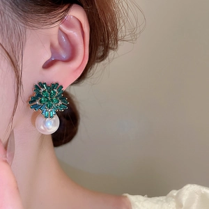 Close-up of gold earrings with green starburst gemstones and a large white pearl drop