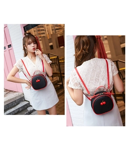 Black round mini cherry backpack shown on a model with red shoulder straps and litchi texture