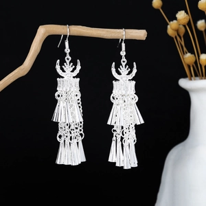 Detail of silver tassel earrings with ethnic horn totem hanging on a wooden branch