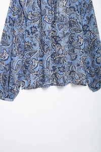 Dettaglio della camicetta in chiffon blu con stampa paisley e piccoli bottoni dorati tondi