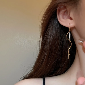 Detail of elegant gold spiral tassel chain earrings on ear for a minimalist jewelry look