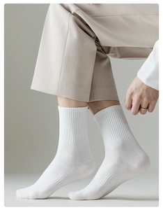 Detail of white cotton crew socks with ribbed texture worn by a model in light beige trousers
