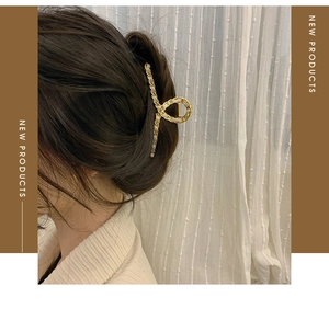 Detail of woven light ribbon on a gold metal hollow cross hair claw clip for women