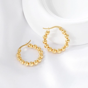 Macro shot of gold beaded hoop earrings on elegant white silk and ceramic background