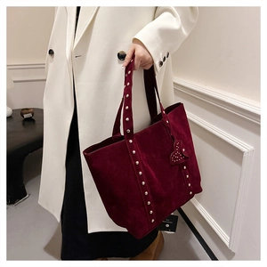Detail of burgundy suede tote bag featuring silver rivets and a heart-shaped charm accessory