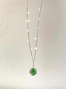 Détail du pendentif en gemme verte dans un filet argenté avec cordon de pierre blanche