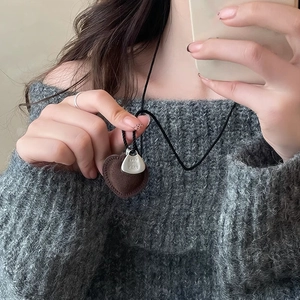 Detail of a brown heart pendant and silver tag on a black braided cord necklace