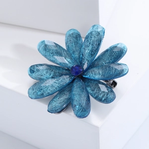 Detail of blue acrylic flower brooch with translucent petals and dark blue gem center