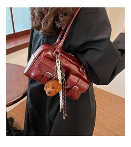 Detail of burgundy patent leather bag featuring plush puppy charm and metal buckle accents