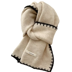 Beige knitted scarf with black stitched borders and est move label on a white background
