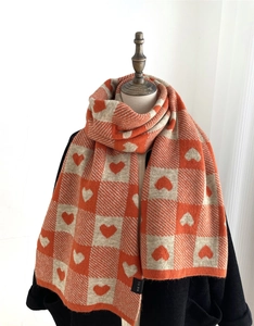Detail of soft knit scarf featuring orange checkerboard and heart patterns on a mannequin