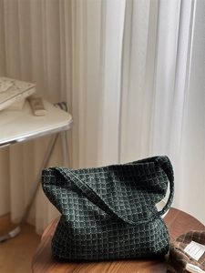 Detail of dark green plaid tweed shoulder bag with woven texture on a wooden stool