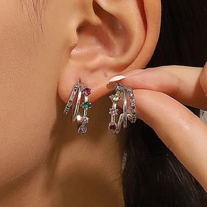 Close-up of layered silver-toned C-shaped earrings with colorful sparkling zircons