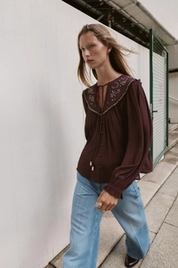 Detail of white embroidery on dark red long-sleeve blouse with neckline tie and collar