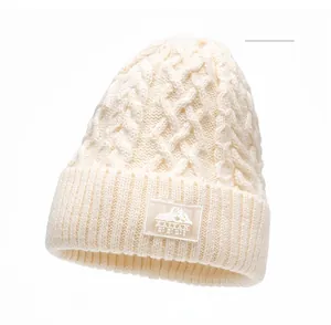 Dettaglio del berretto in maglia a trecce beige con toppa logo montagna e trama calda