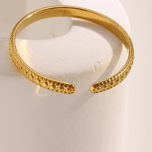 Close-up of a 18K gold-plated stainless steel ring with textured relief on white base