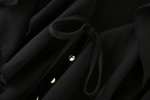 Détail du tissu en mousseline noire avec boutons dorés et nœud papillon à l'encolure