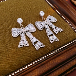 Detail of silver bow earrings with sparkling clear stones on dark green velvet padding