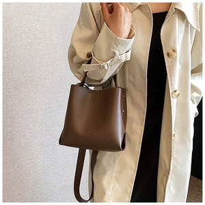 Brown leather bucket bag styled on shoulder with beige trench coat for a chic urban look