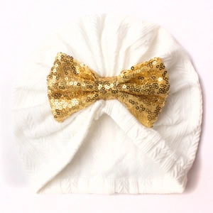 White baby beanie with a sparkling gold sequin bow detail on a knitted turban cap