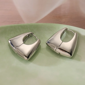 Elegantes pendientes geométricos plateados de corazón en un plato de cerámica