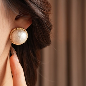 Close-up of elegant gold-plated cotton pearl round earrings worn by a model