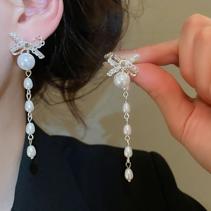 Close-up of dangling bow earrings with crystal inlay and baroque pearl tassels