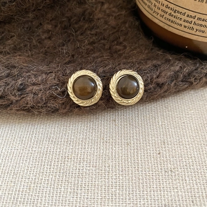 Detail of vintage gold-rimmed round tiger eye earrings on warm textured knit background