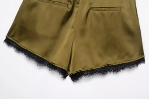 Detail der olivgrünen Satin-Shorts mit feinem schwarzem Spitzenbesatz und Taschnähten