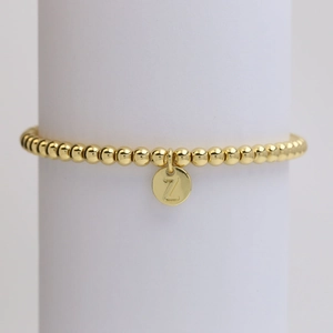 Detailed shot of golden bead bracelet featuring a round pendant engraved with letter Z