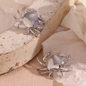 Detailed view of crab-shaped earring in silver finish on a textured stone background