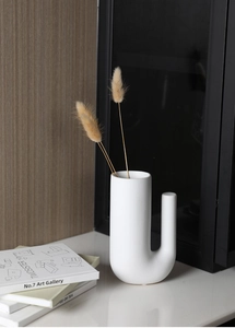 Détail d'un vase moderne en céramique blanche mate en forme de J avec fleurs séchées