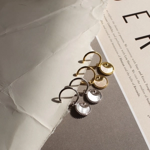 Detalle de los pendientes de moneda en oro de 18K y plata con nácar y textura solar