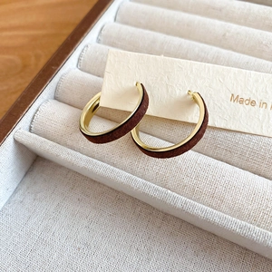 Close-up of C-shaped earrings with gold metal edges and dark brown velvet inlay details