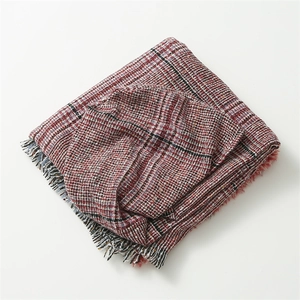 Detailed view of red plaid woven fabric and tassel fringe edge on the hooded poncho