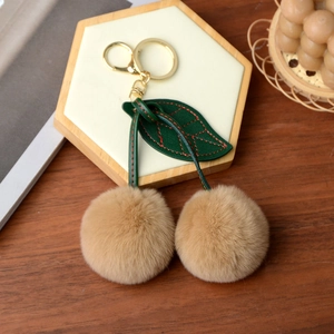 Close-up of fluffy khaki faux fur cherry keychain with green leather leaves on tray