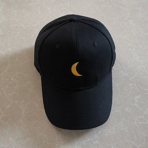 Top view of a black cotton baseball cap featuring detailed yellow moon embroidery