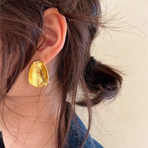 Irregular textured gold oval stud earrings in 925 silver worn by a model in a close-up view