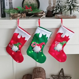 Three felt Christmas stockings with LED lights and gnome motif reading JOY on fireplace