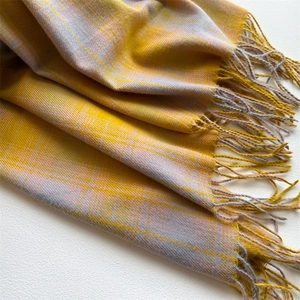 Close-up of yellow and grey plaid scarf showing soft cashmere-like texture and tassel detail