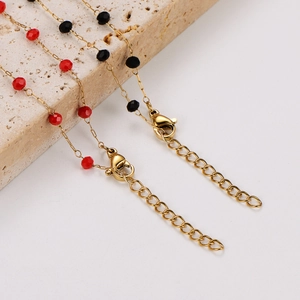 Detailed view of gold chain necklaces with red and black faceted beads on stone