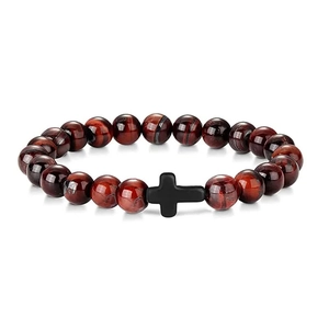 Macro detail of red tiger eye beads with a black cross charm on an elastic bracelet
