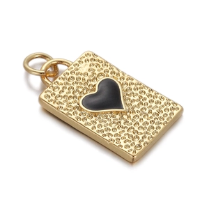 Macro detail of a golden rectangular pendant with hammered texture and black enamel heart
